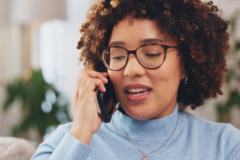 Woman with curly hair and glasses talking on the phone.