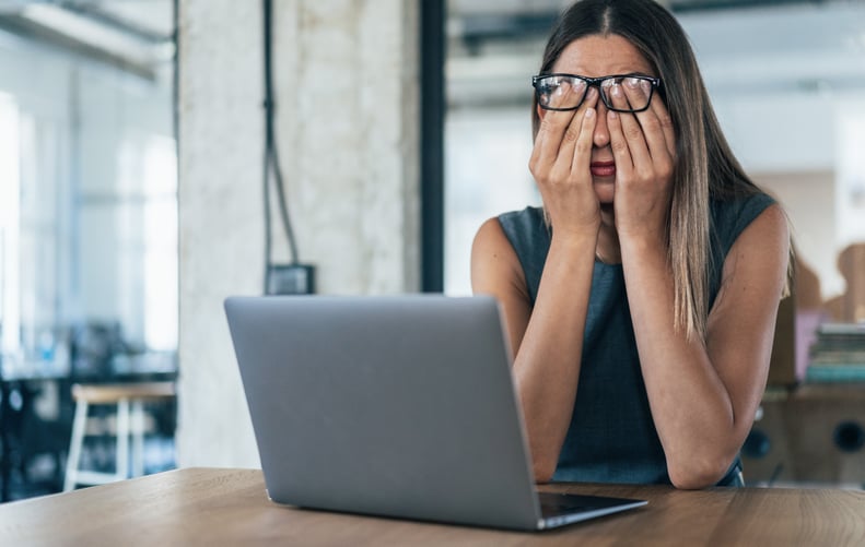 Business woman rubbing her irritated eyes under her glasses while sitting in front of her computer