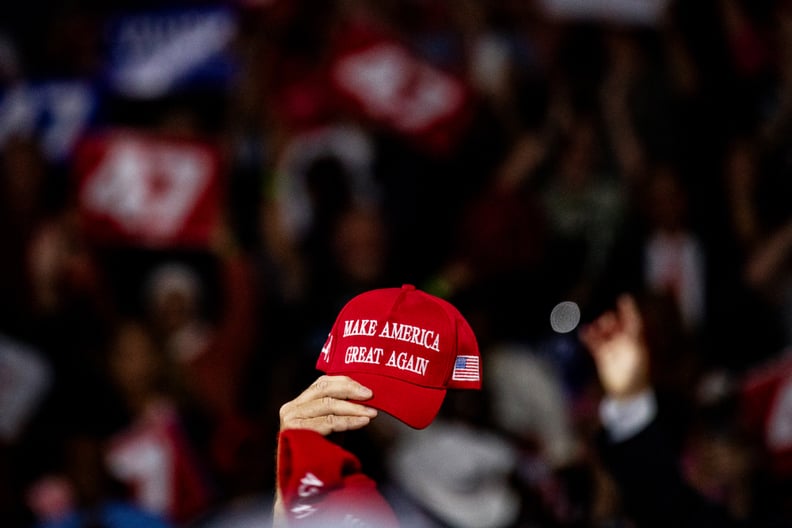 Trump rally attendee waves Make America Great Again hat in the air.