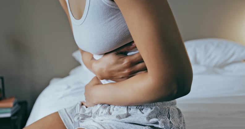 Woman in bedroom with arms wrapped around her stomach, painful bloating after sex.