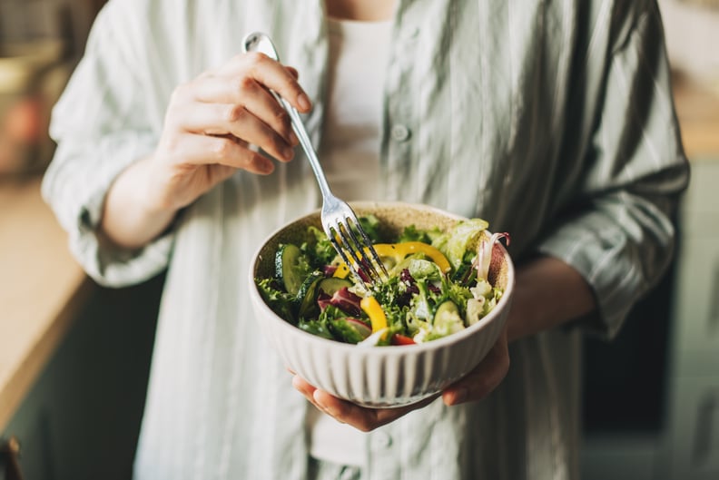 Woman holding bowl with lettuce, bell peppers, and cucumbers.